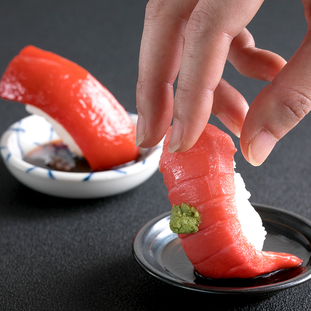 これは元祖食品サンプル屋の「つまみ寿司 マグロ」の手でつまむ瞬間の商品イメージ画像です。